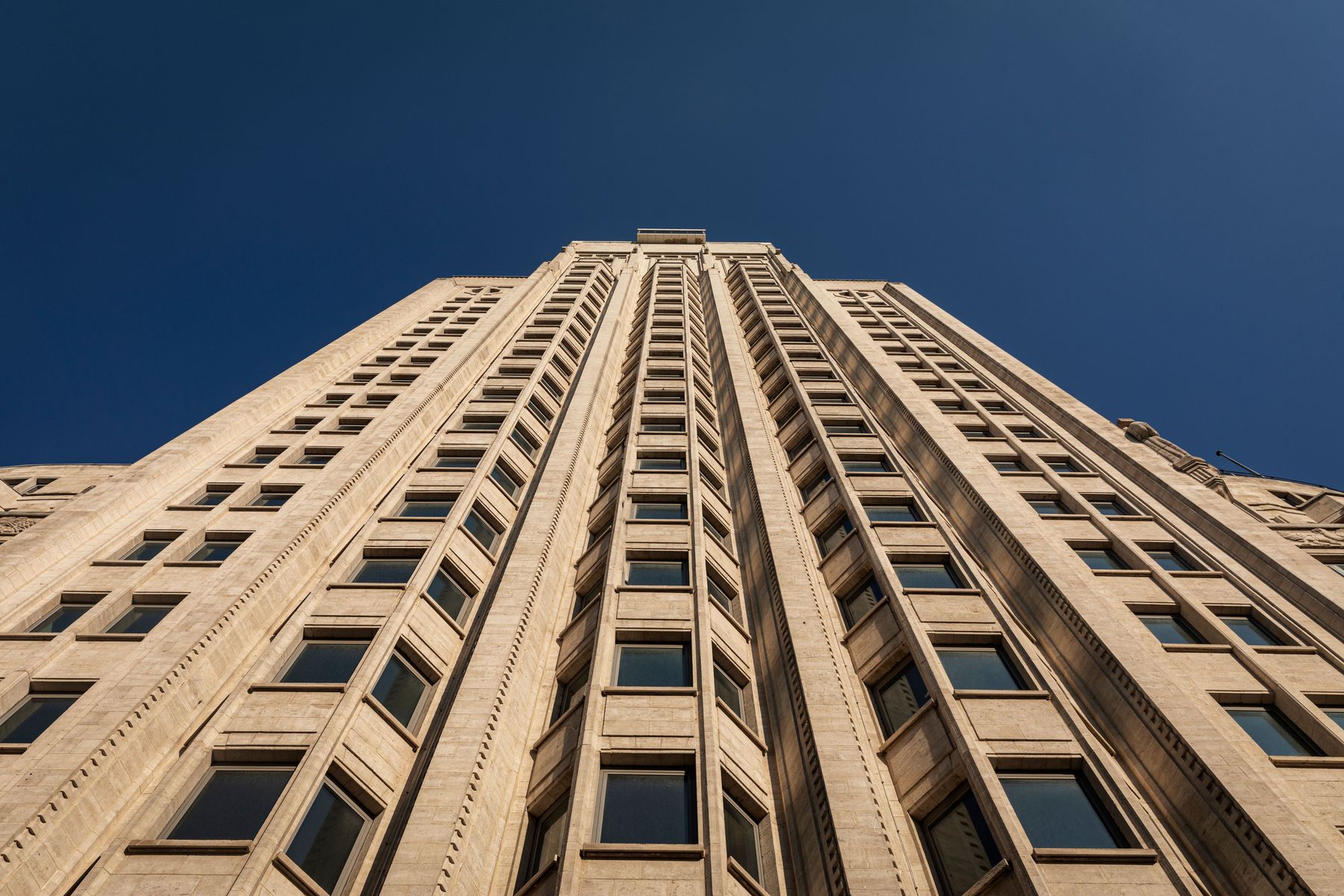 Frontaal zicht op de Boerentoren tussen omliggende gebouwen, met heldere blauwe lucht en tramdraden in beeld