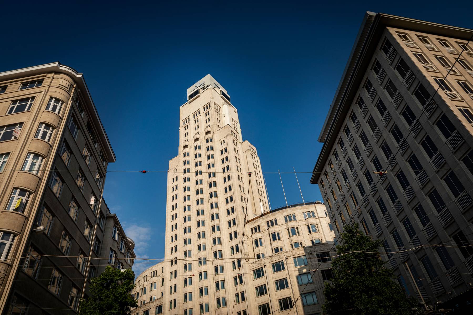 Opwaarts perspectief op de Boerentoren in Antwerpen, met de art-decogevel die steil omhoog rijst tegen een blauwe lucht.