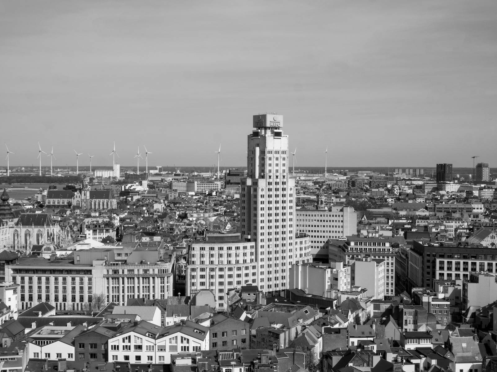 Zwart-wit panoramafoto van Antwerpen met de Boerentoren centraal in het stadsbeeld, omringd door daken en gebouwen.
